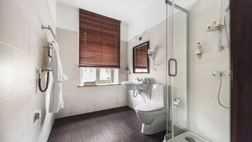 Ein modernes Badezimmer mit Toilette, Waschbecken und Dusche. An den Fenstern befinden sich Holzjalousien, und ein Handtuchhalter ist zu sehen.