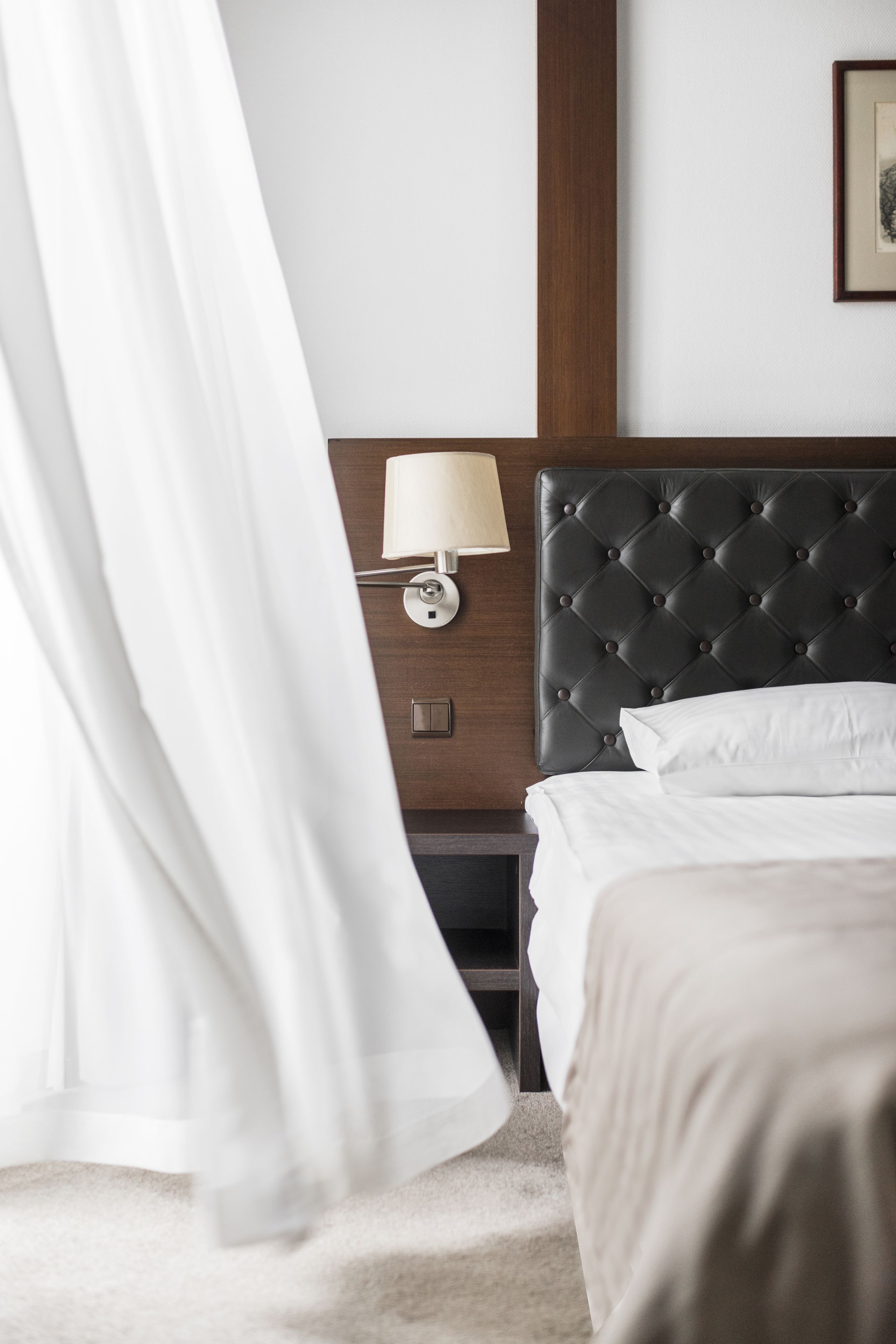 A hotel room with a tufted headboard, a bedside lamp, a bed with white linens, and a wooden nightstand.