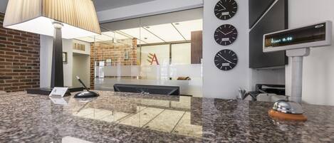 A modern reception area with a granite counter, a lamp, clocks, and a digital display.