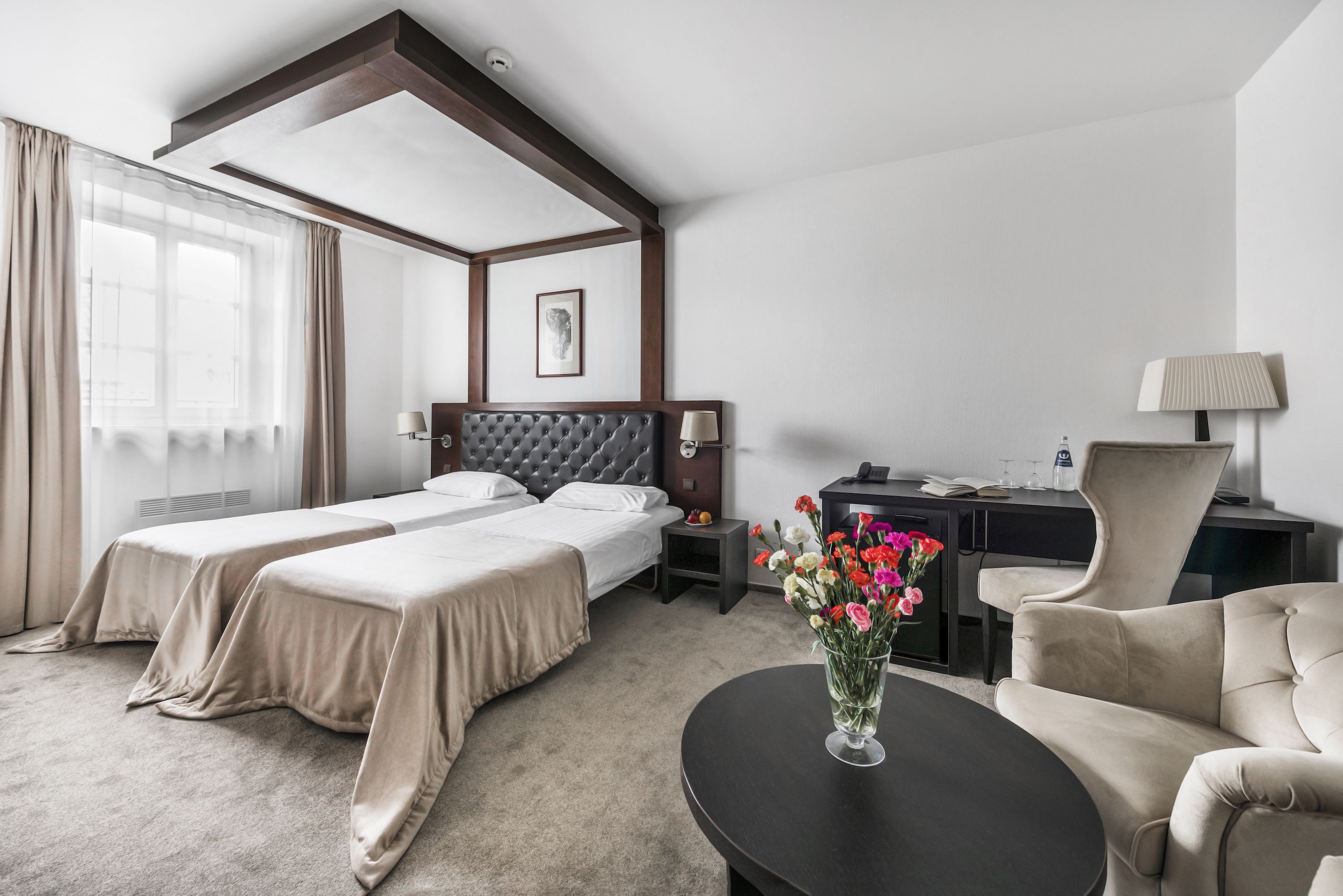 A hotel room with two beds, a desk, a chair, a coffee table, and a vase of flowers.