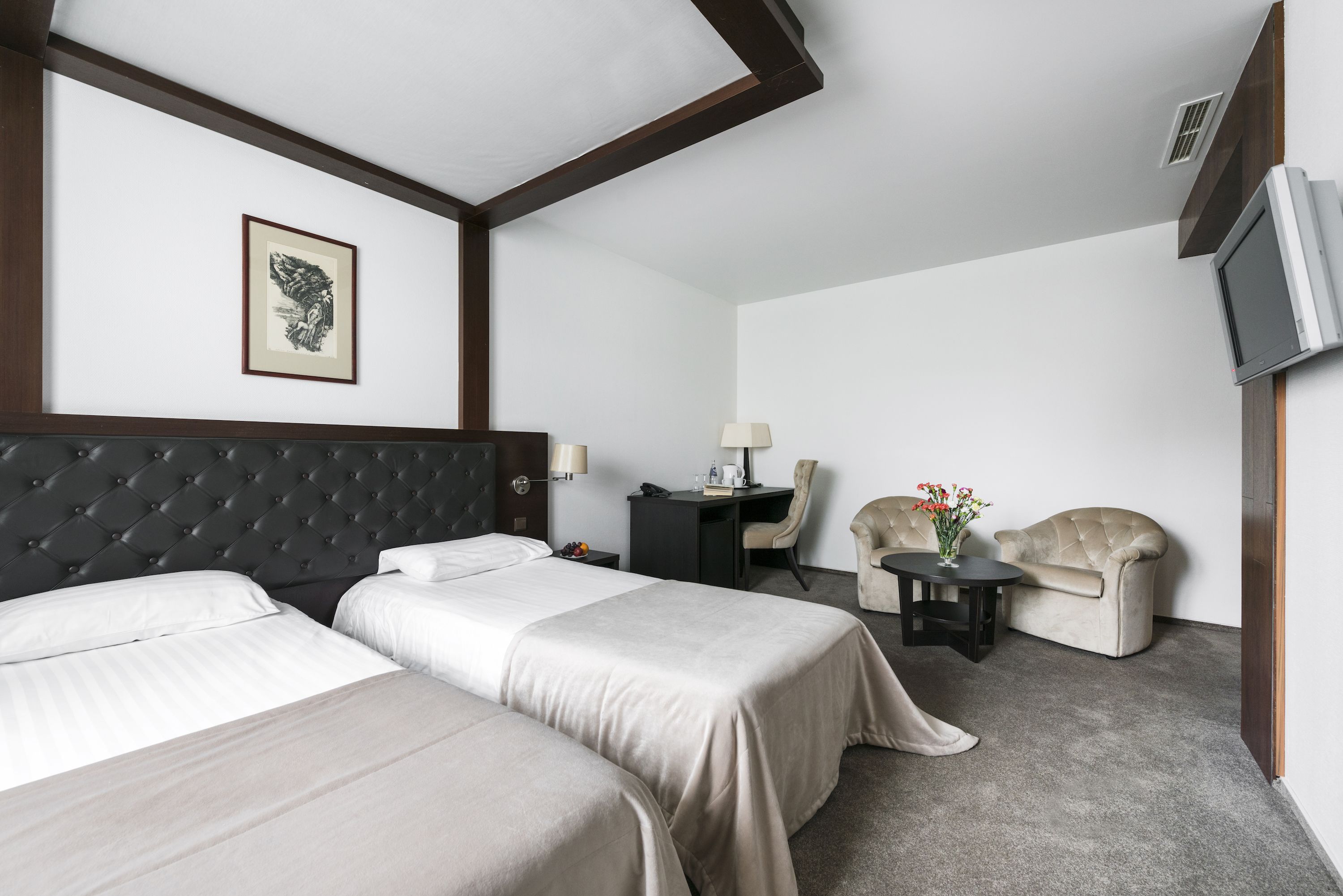 Une chambre d’hôtel avec deux lits, un bureau, une chaise, une télévision et un tableau encadré au mur.