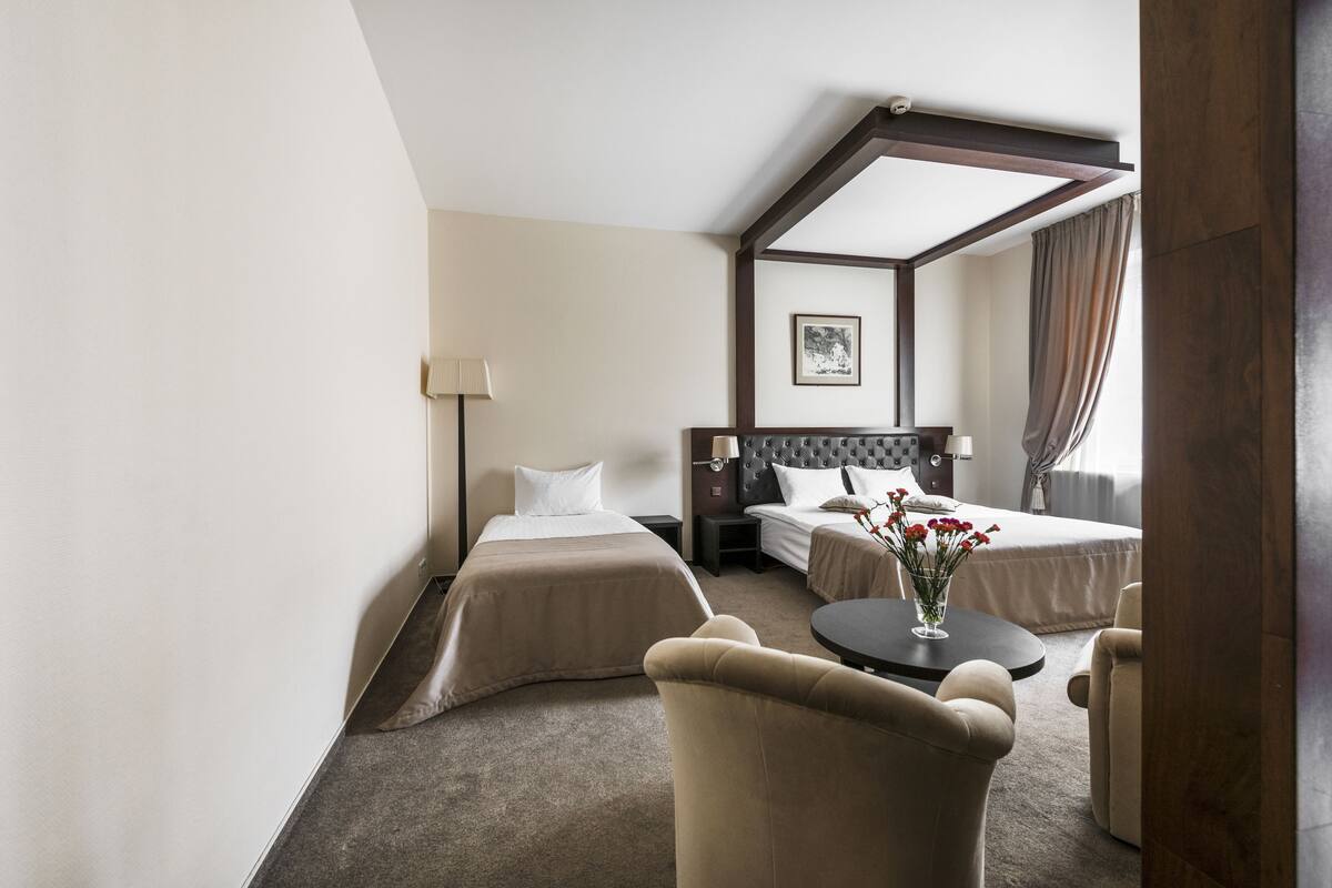 Une chambre d’hôtel avec deux lits, un coin salon avec une table et des chaises, une lampe et un tableau encadré au mur.