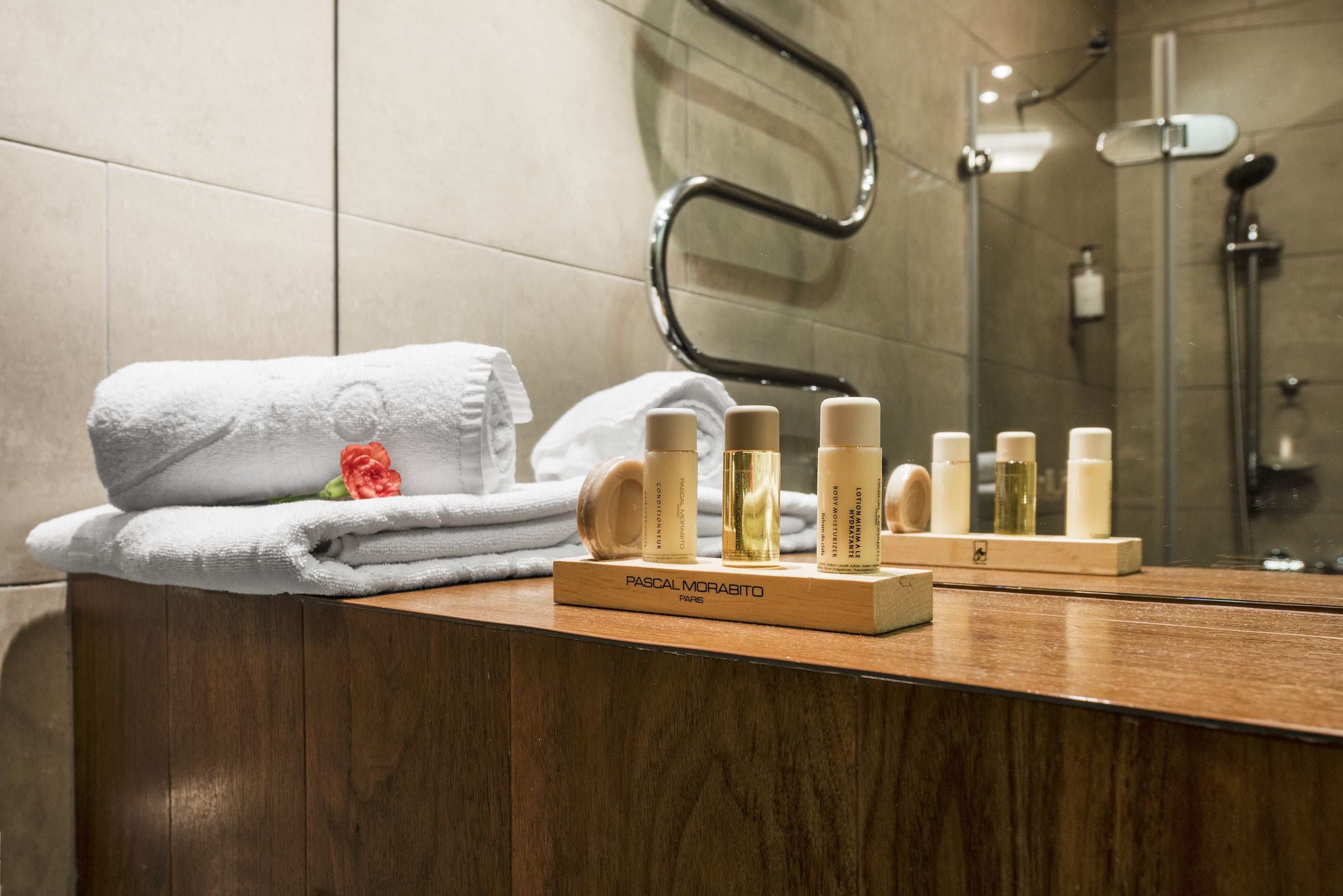 A bathroom with a wooden vanity, a towel rack with folded towels, and a set of toiletries on a wooden tray labeled "PASCAL MORABITO PARIS".