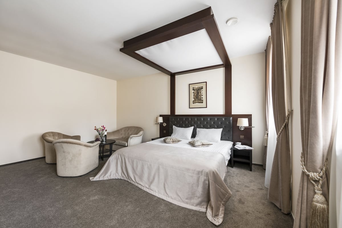 Une chambre d’hôtel avec un grand lit, deux tables de chevet, une chaise et une petite table sur laquelle est posé un vase de fleurs.