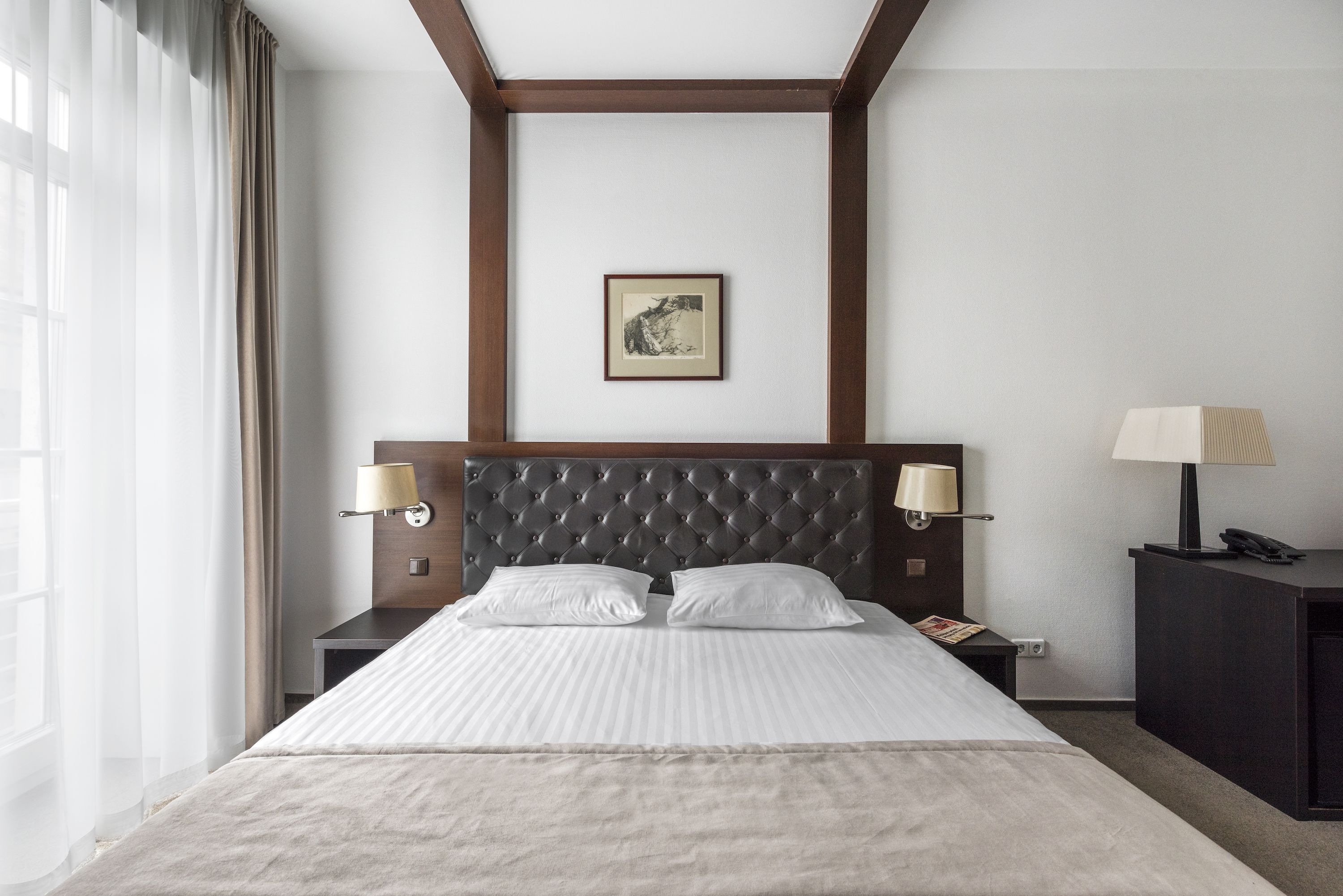 Ein Hotelzimmer mit einem großen Bett, zwei Nachttischen mit Lampen, einem gerahmten Bild an der Wand und einem Fenster mit Vorhängen.