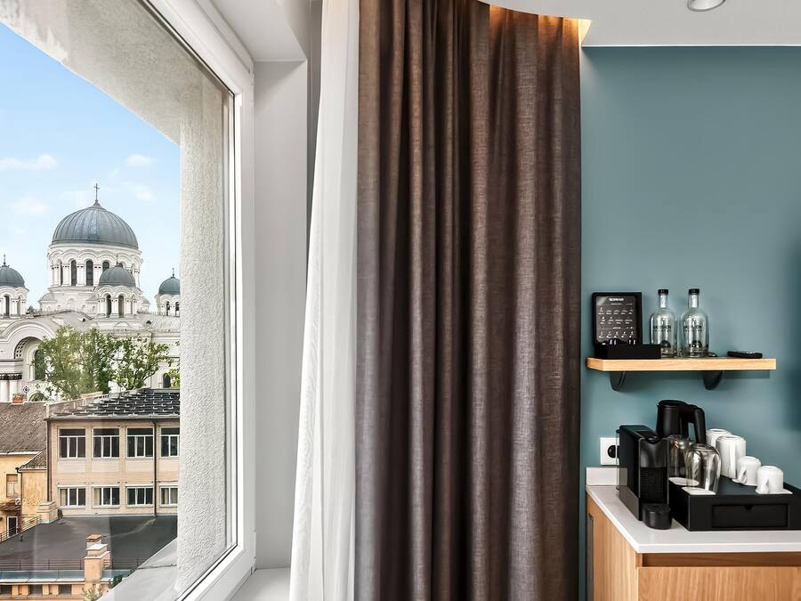 Una habitación con vistas a un edificio histórico con cúpulas, una ventana con cortinas y una kitchenette equipada para preparar café.