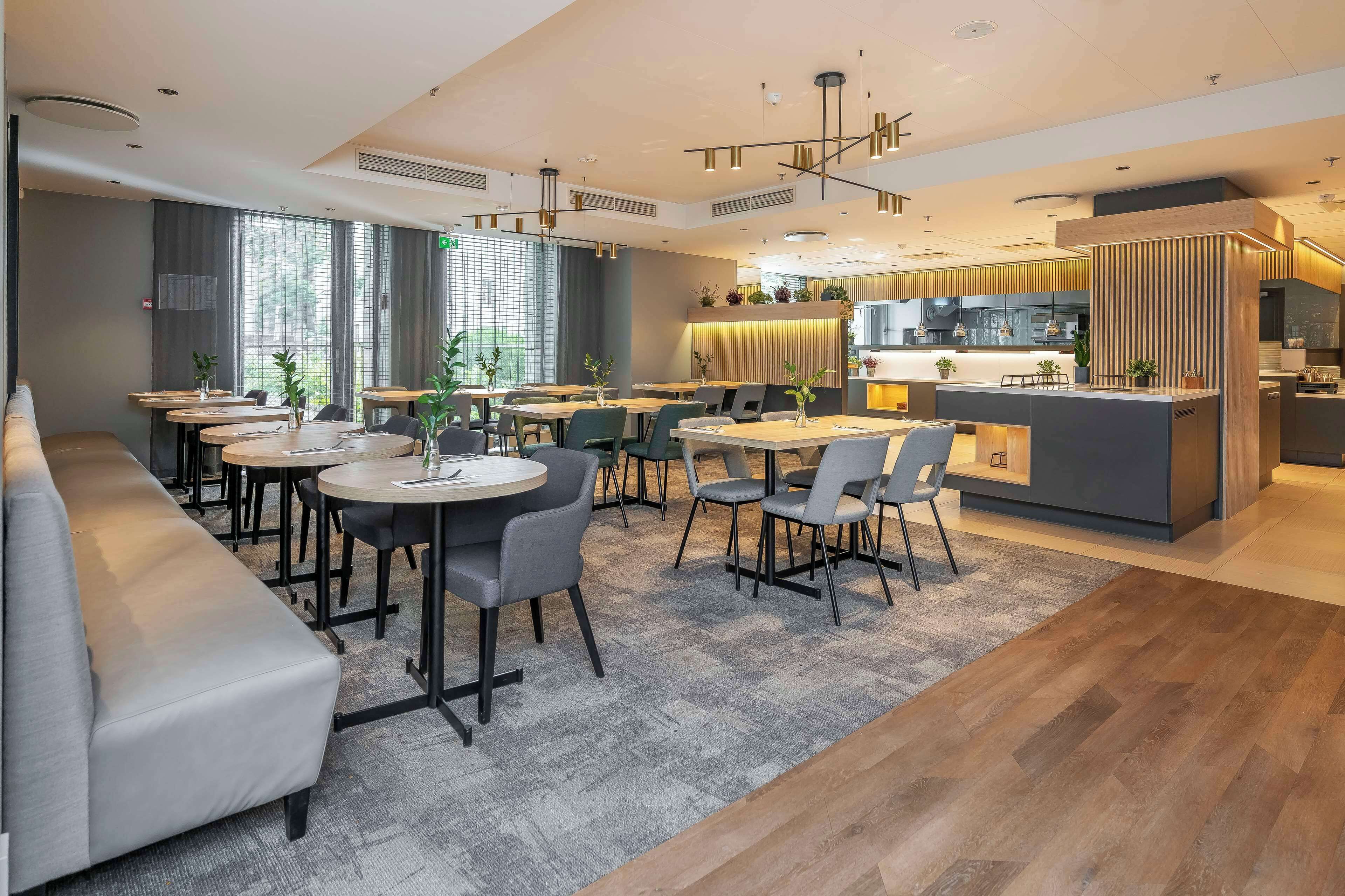 A modern restaurant with a long counter, multiple tables, and a seating area with a sofa.