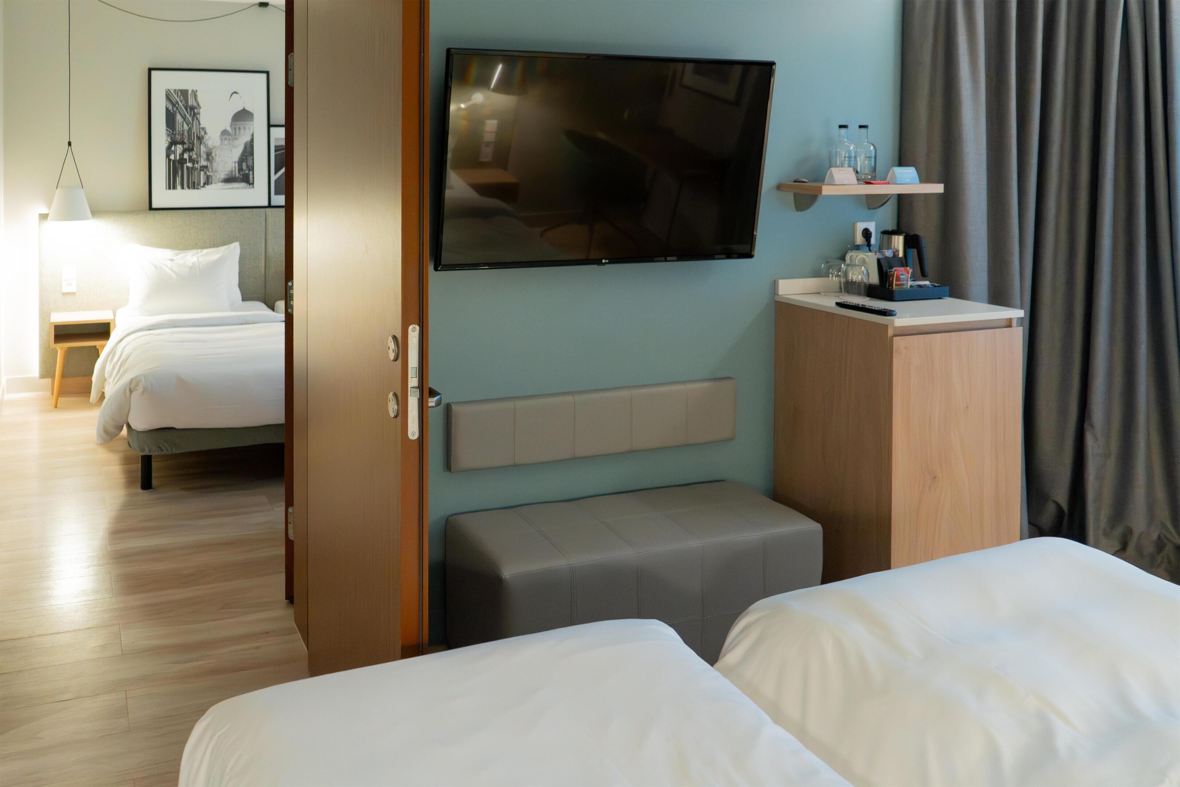 A hotel room with a bed, a TV mounted on the wall, a bedside table, and a small seating area.