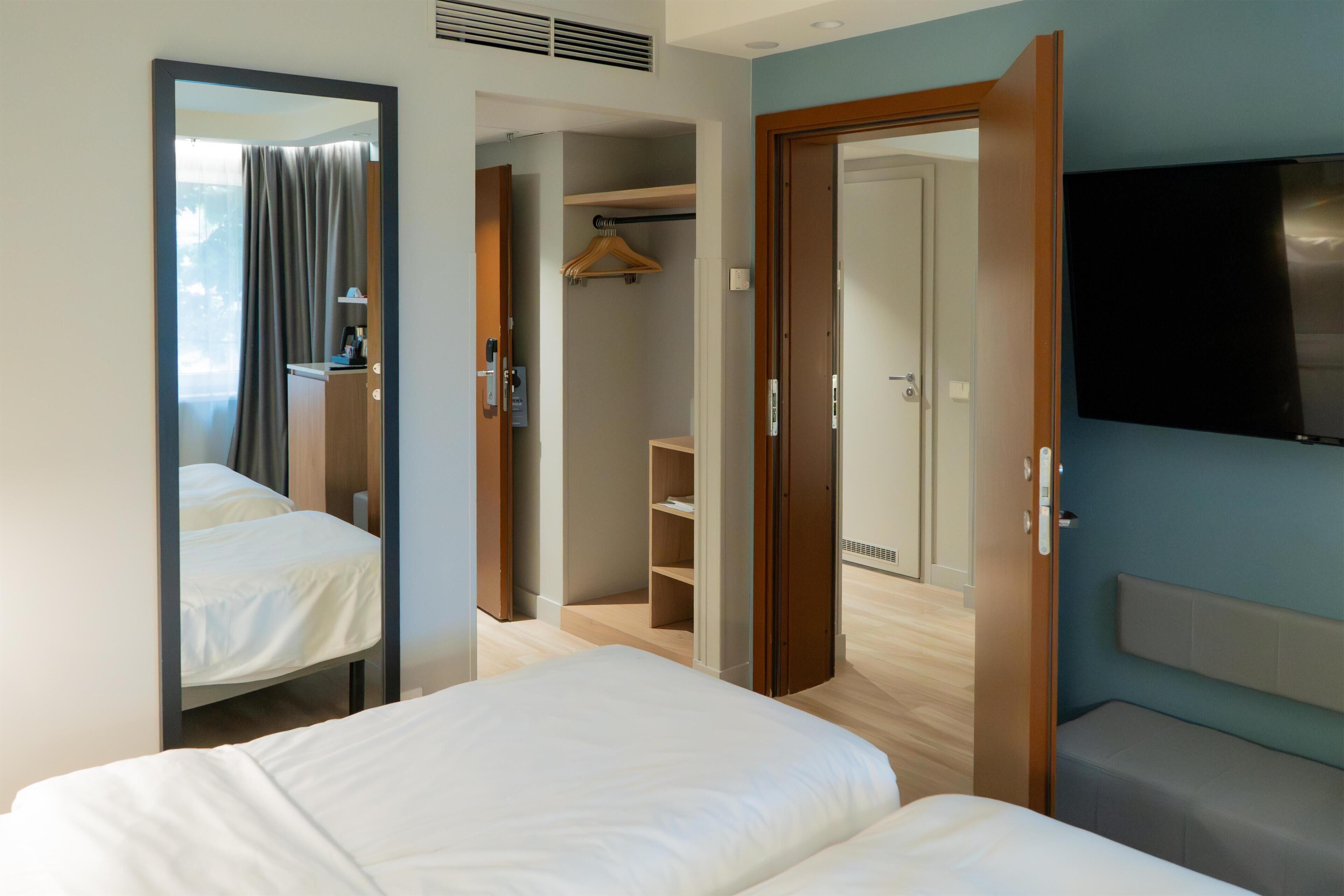 Een hotelkamer met een bed, een spiegel, een kledingkast, een televisie en een badkamer.