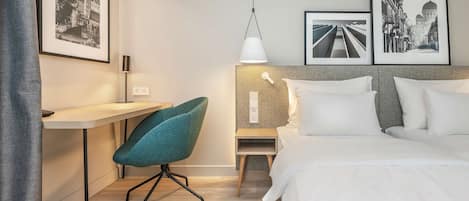 A hotel room with a bed, a desk, a chair, and two framed pictures on the wall.