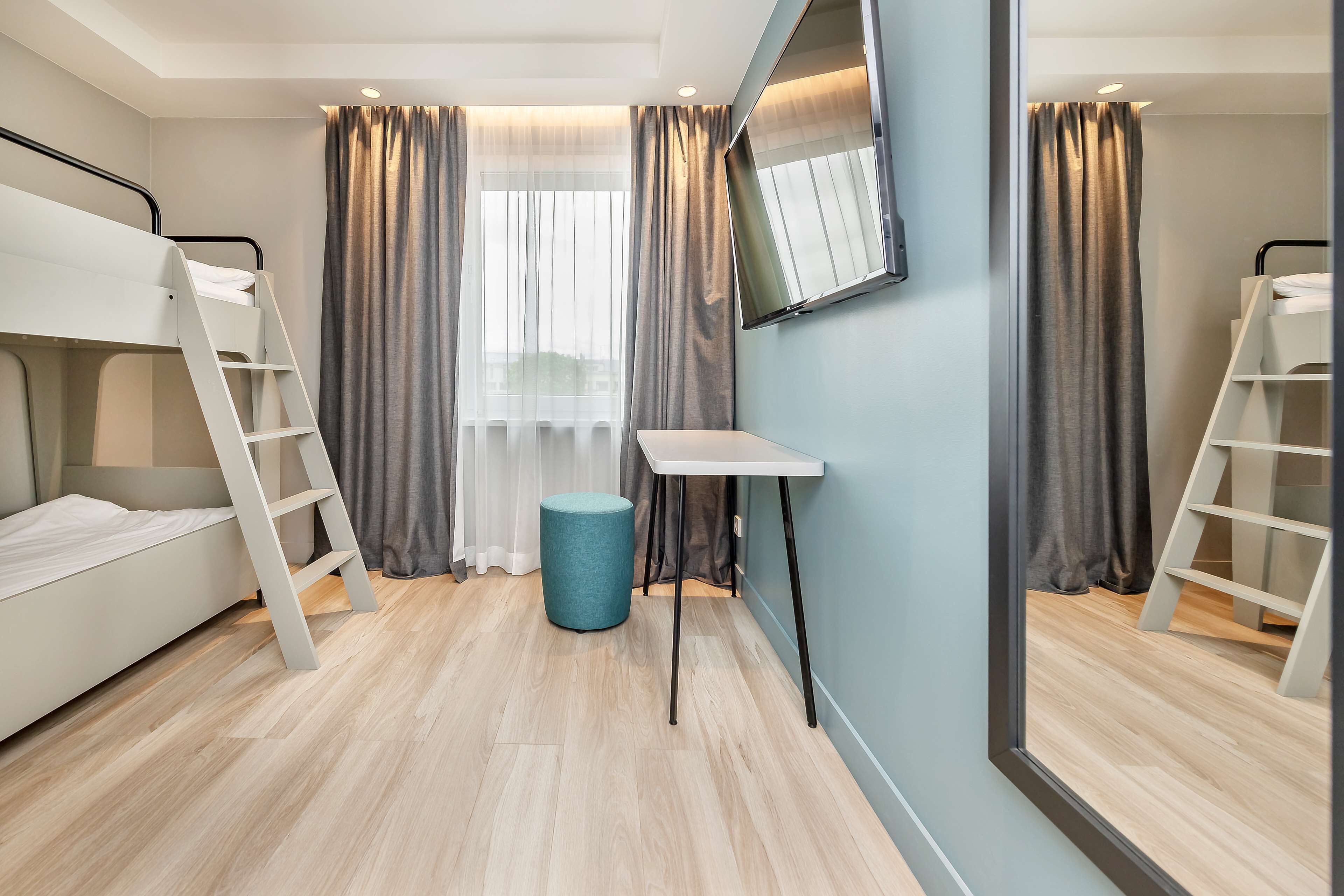 A room with bunk beds, a desk, a chair, and a round ottoman.