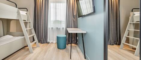 A room with bunk beds, a desk, a chair, and a round ottoman.