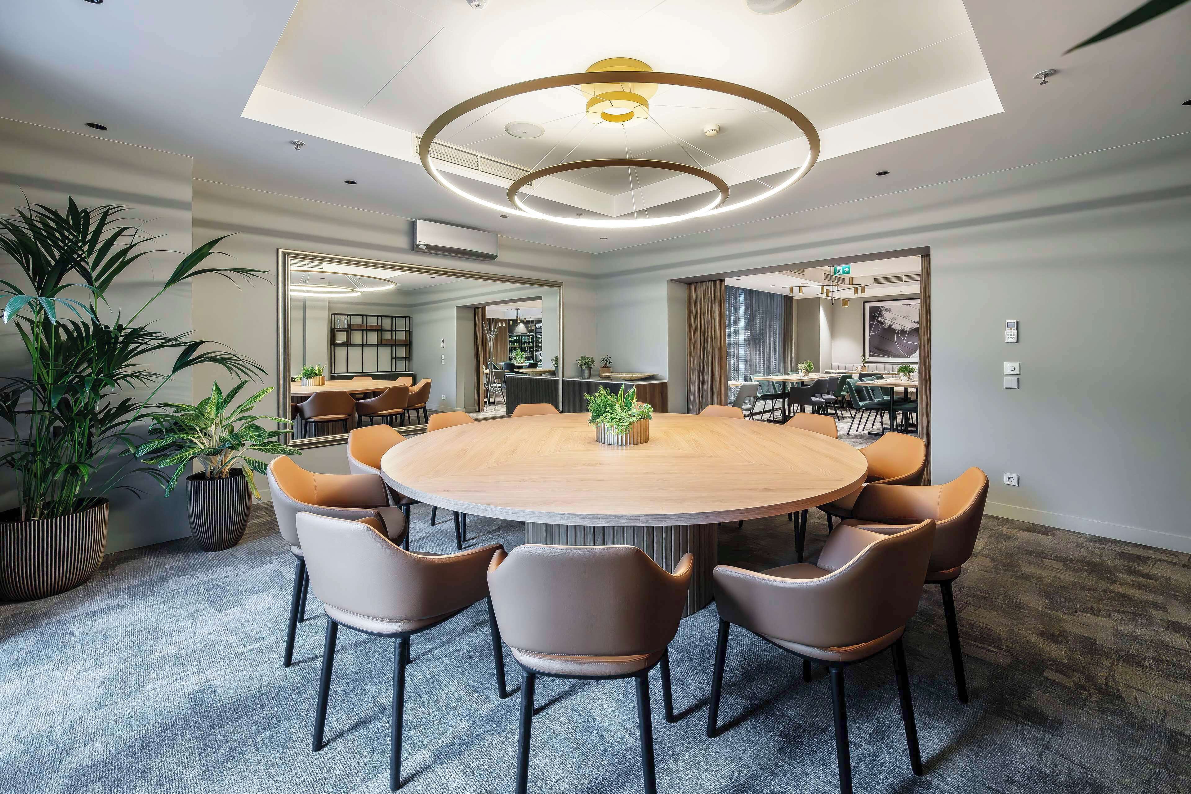 A modern conference room with a round table, comfortable chairs, and a ceiling light fixture.