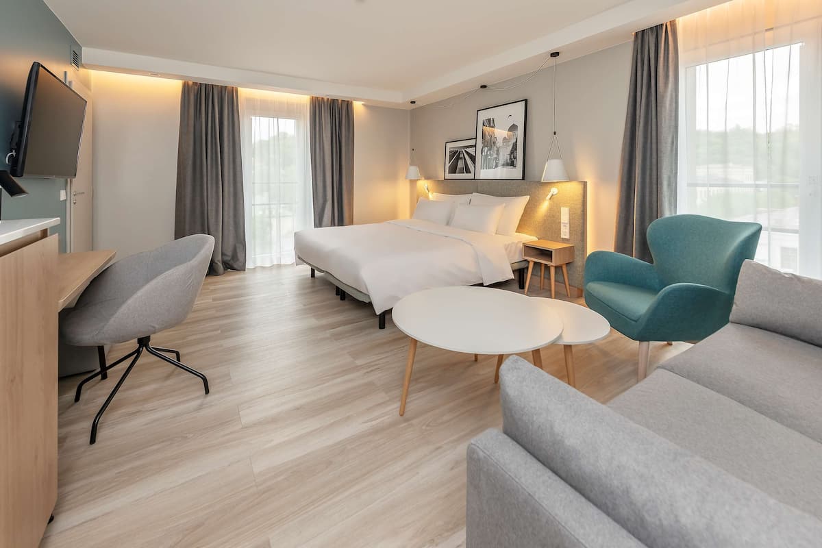 A modern hotel room with a bed, a desk, a chair, a sofa, and a small table.