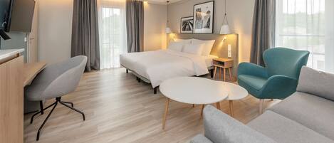 Una habitación de hotel moderna con una cama, un escritorio, una silla, un sofá y una mesita.
