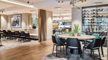 Een moderne eetruimte met een ronde tafel, zwarte stoelen en een houten vloer. Er is een bar met flessen op de planken en een groot raam.