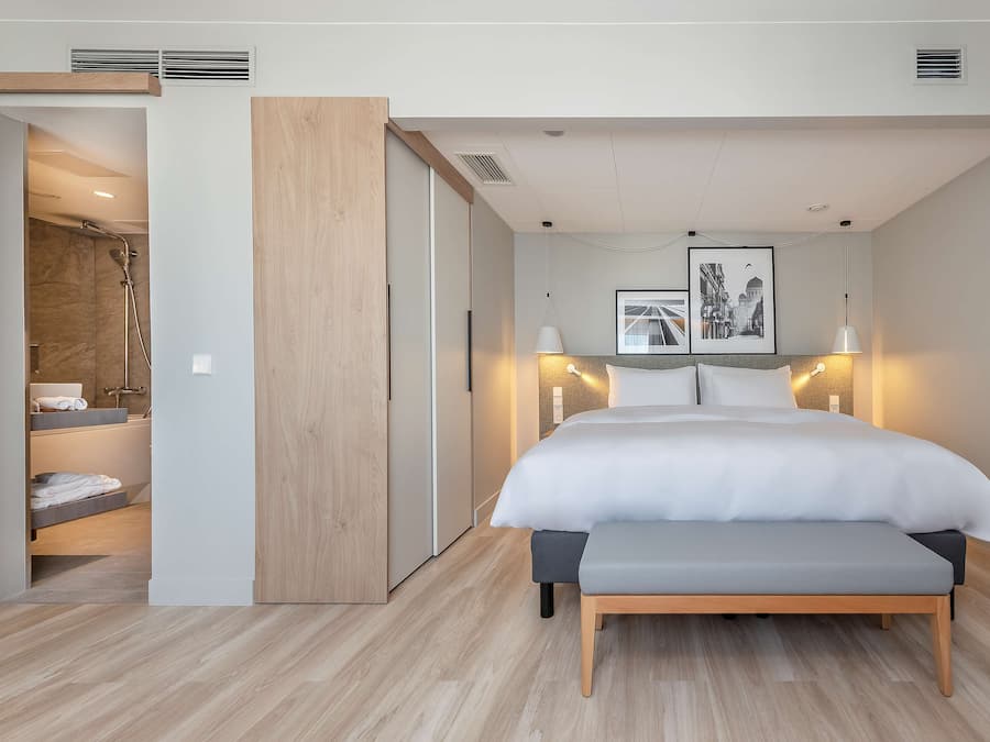 A modern bedroom with a large bed, bedside lamps, a bench, and a walk-in closet.