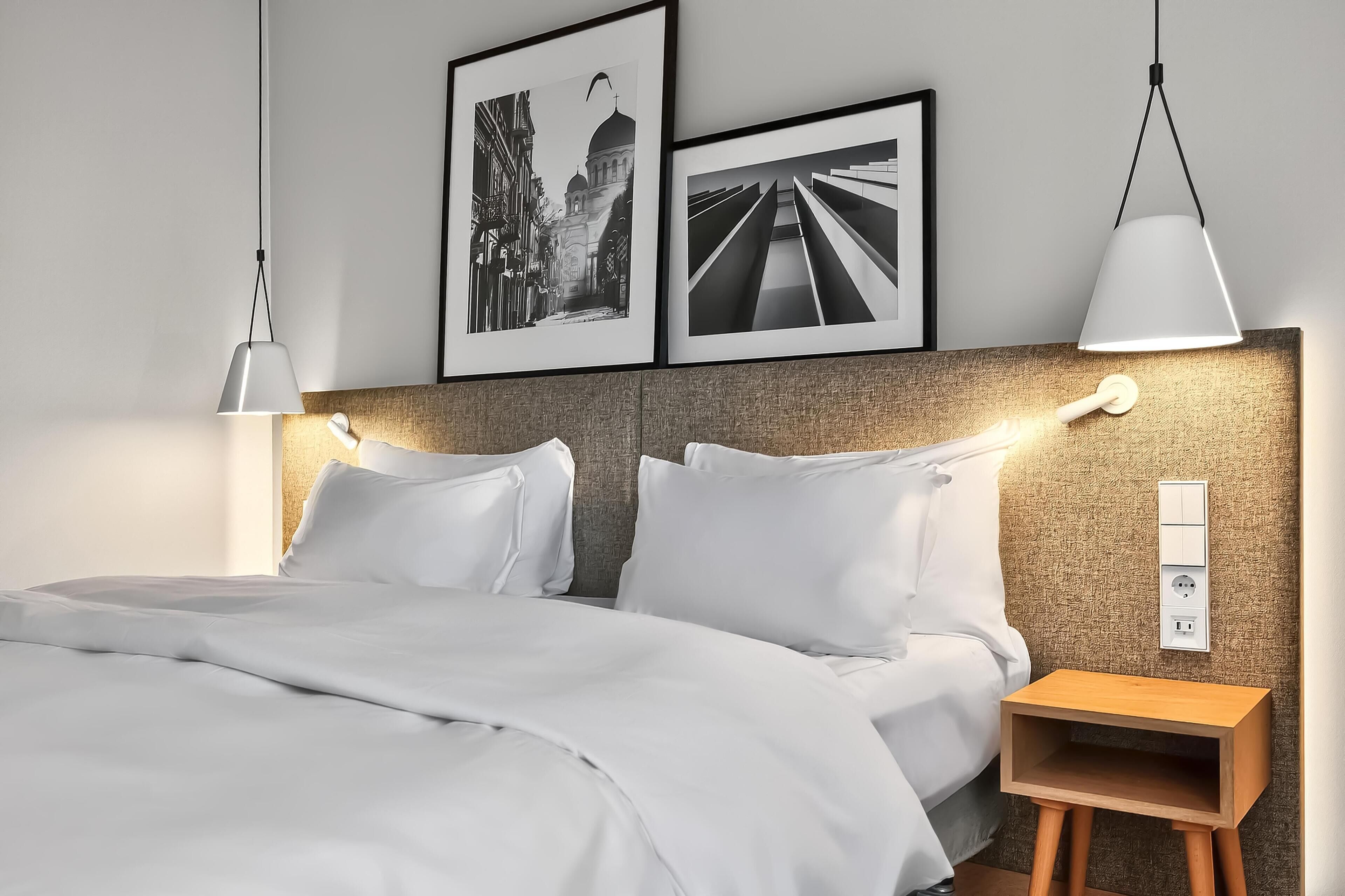 A neatly made bed with white linens, a headboard with a textured finish, and a bedside table with a wooden finish.
