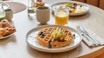 Morgenmad med vafler, blåbær og et glas appelsinjuice på et bord.