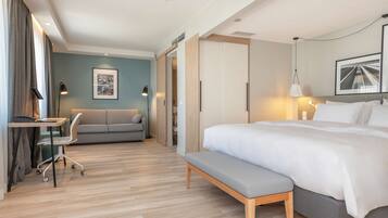 A modern hotel room with a large bed, a desk, a chair, and a sofa.
