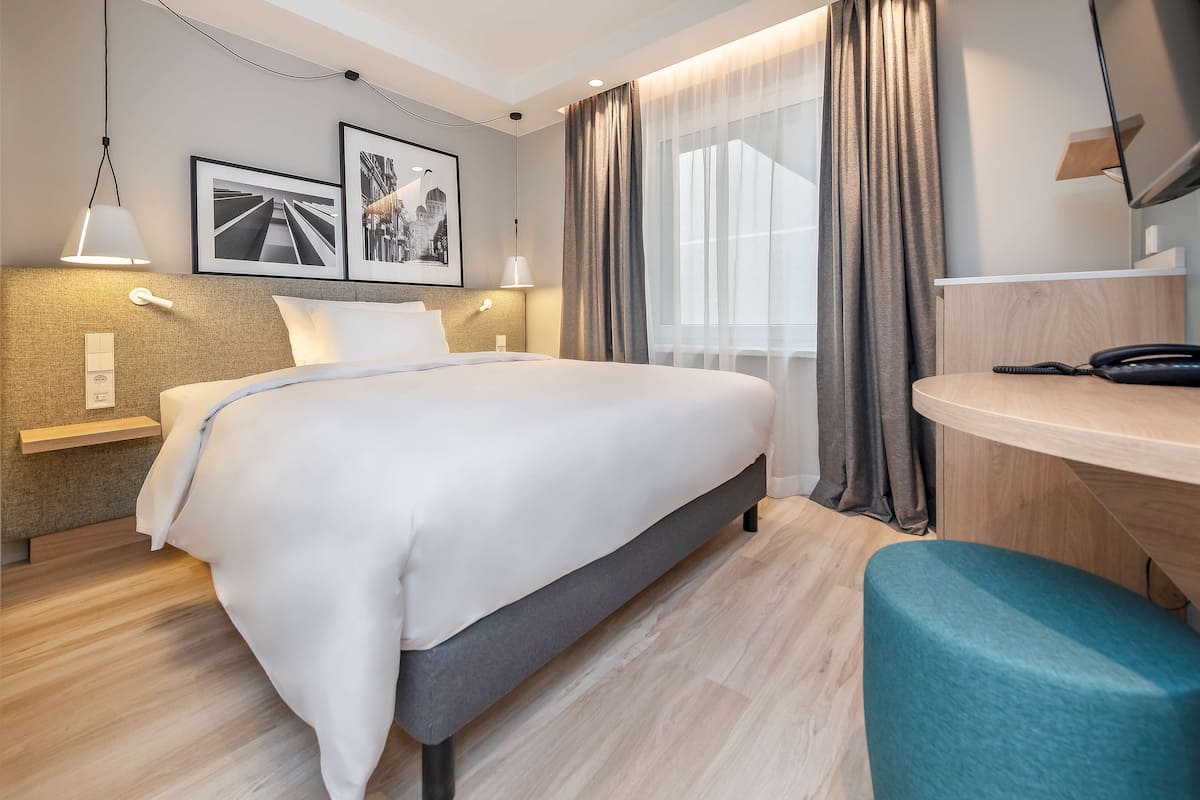 A modern hotel room with a large bed, bedside tables, a desk, and a TV.