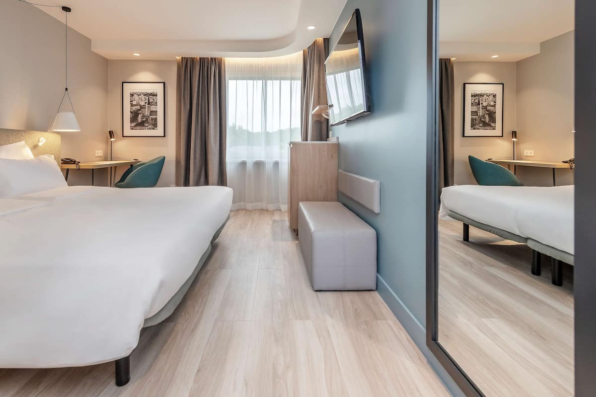 A modern hotel room with two beds, a desk, a bench, and a large mirror.