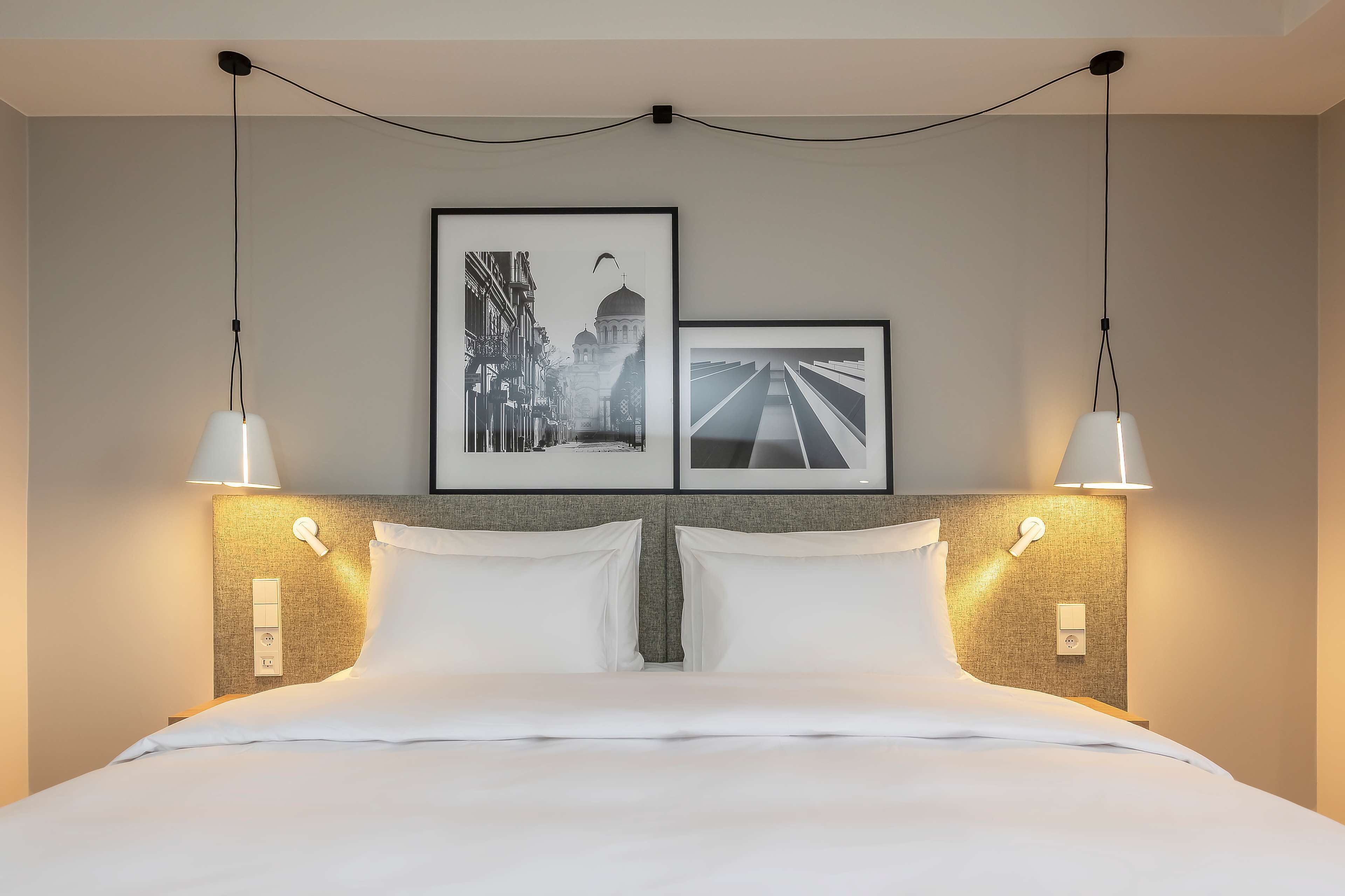 A neatly made bed with white linens, a headboard with a textured pattern, and two wall-mounted light fixtures.