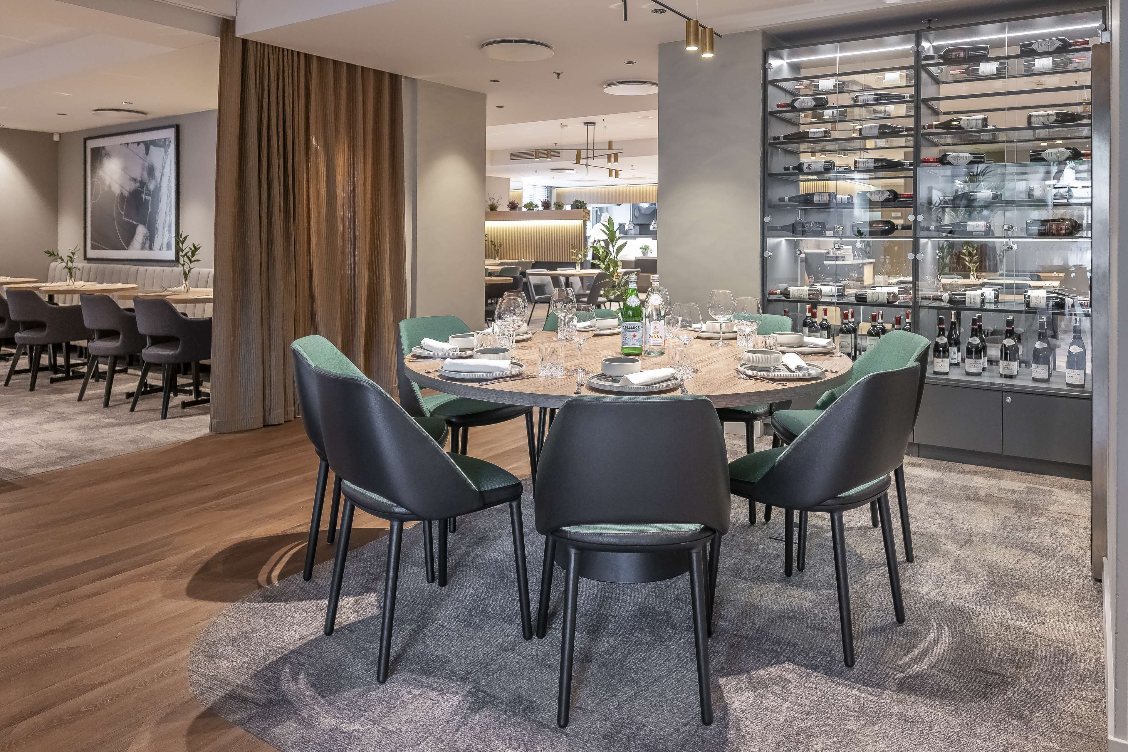 A modern dining area with a round table, black chairs, and a wine display.