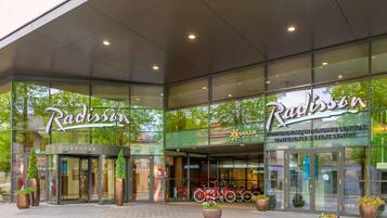L’entrée d’un hôtel Radisson, avec des portes en verre, des plantes en pot et des vélos garés à l’extérieur.