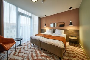 A hotel room with a large bed, a chair, a small table, and a large window.