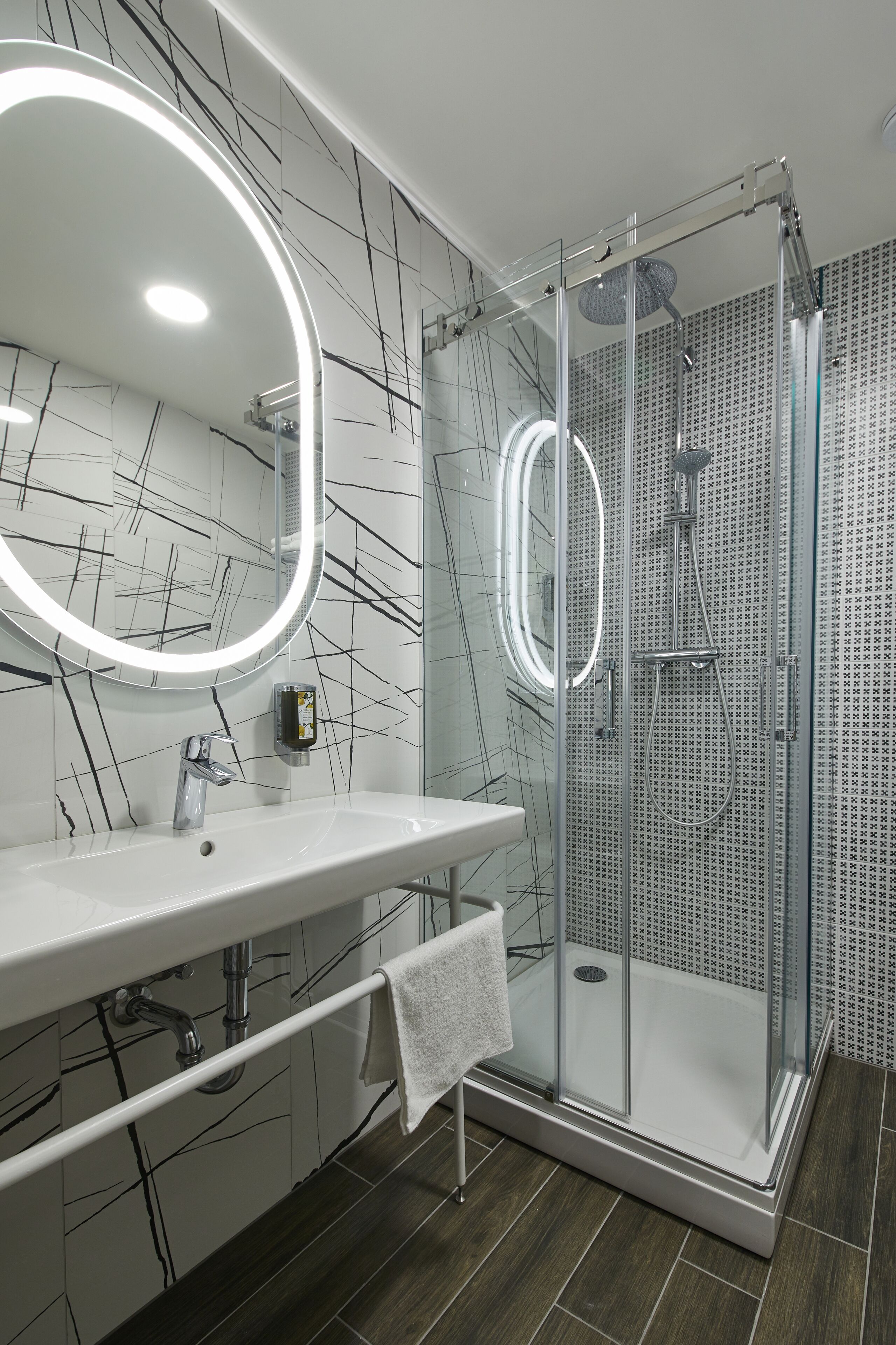A modern bathroom with a glass-enclosed shower, a white vanity with a mirror, and a marble-patterned wall.