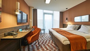 A hotel room with a bed, desk, chair, and a large window. - Hotel Kaunas (Kaunas)