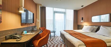 A hotel room with a bed, desk, chair, and a large window.