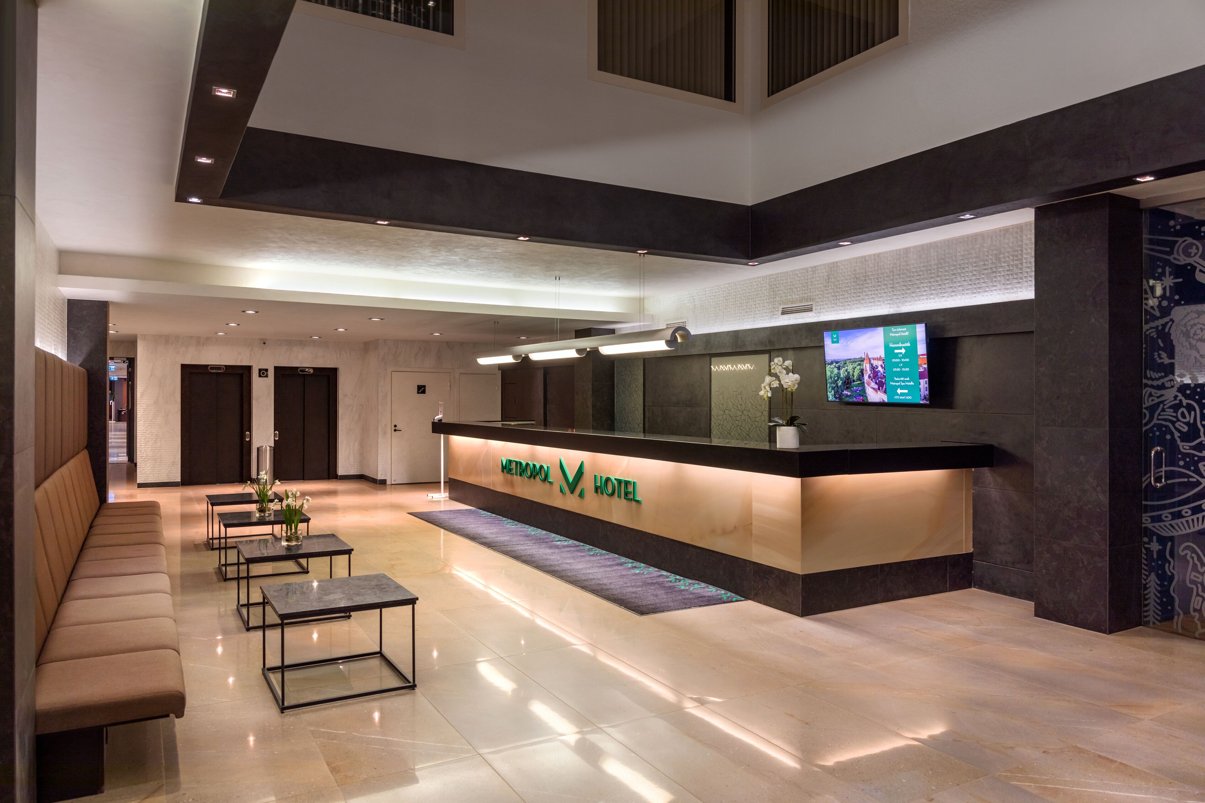 A modern hotel lobby with a reception desk, seating area, and a digital display.