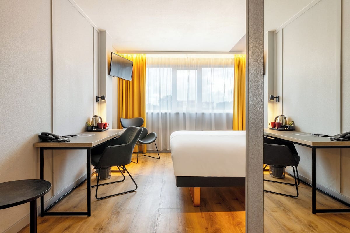 Ein Hotelzimmer mit einem Bett, zwei Schreibtischen, Stühlen, einem Fernseher und einem Fenster mit Vorhängen.