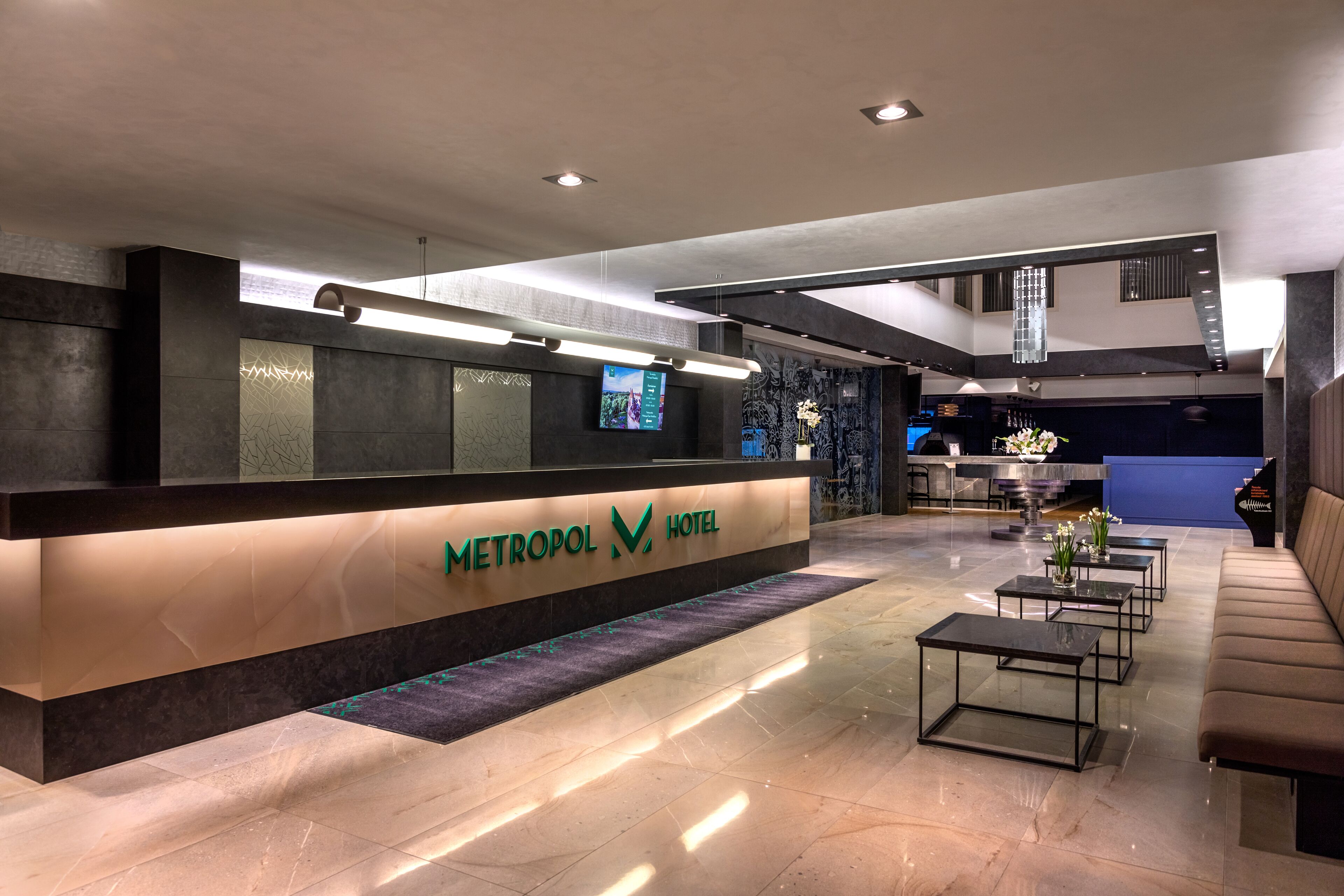 A hotel reception area with a modern design, featuring a reception desk, seating area, and a staircase.
