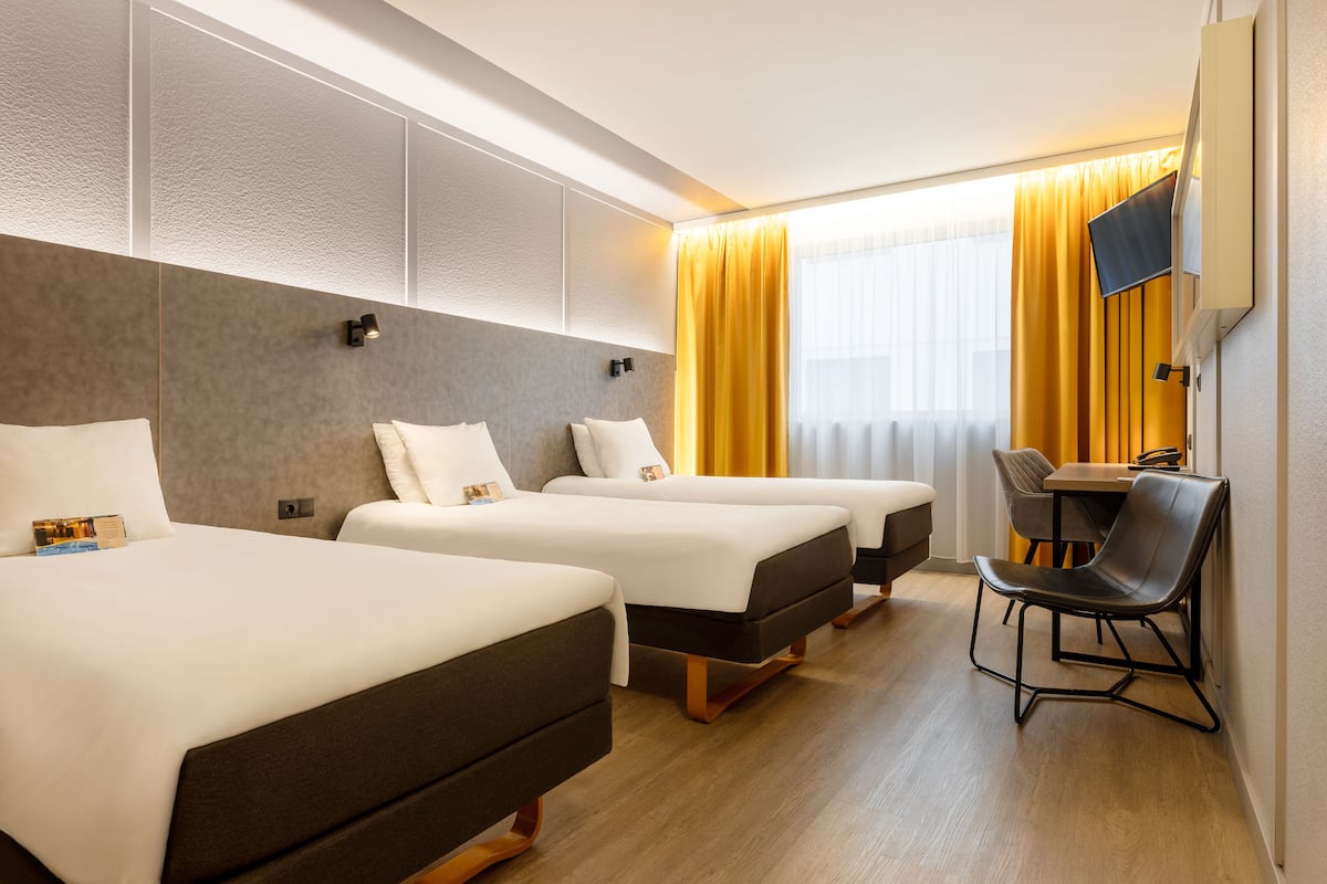 Ein Hotelzimmer mit drei Betten, einem Schreibtisch und einem Stuhl.