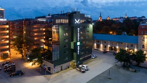 A modern hotel with a prominent 'V' logo, multiple floors, and a parking area. - Hotel Metropol (Tallinn)