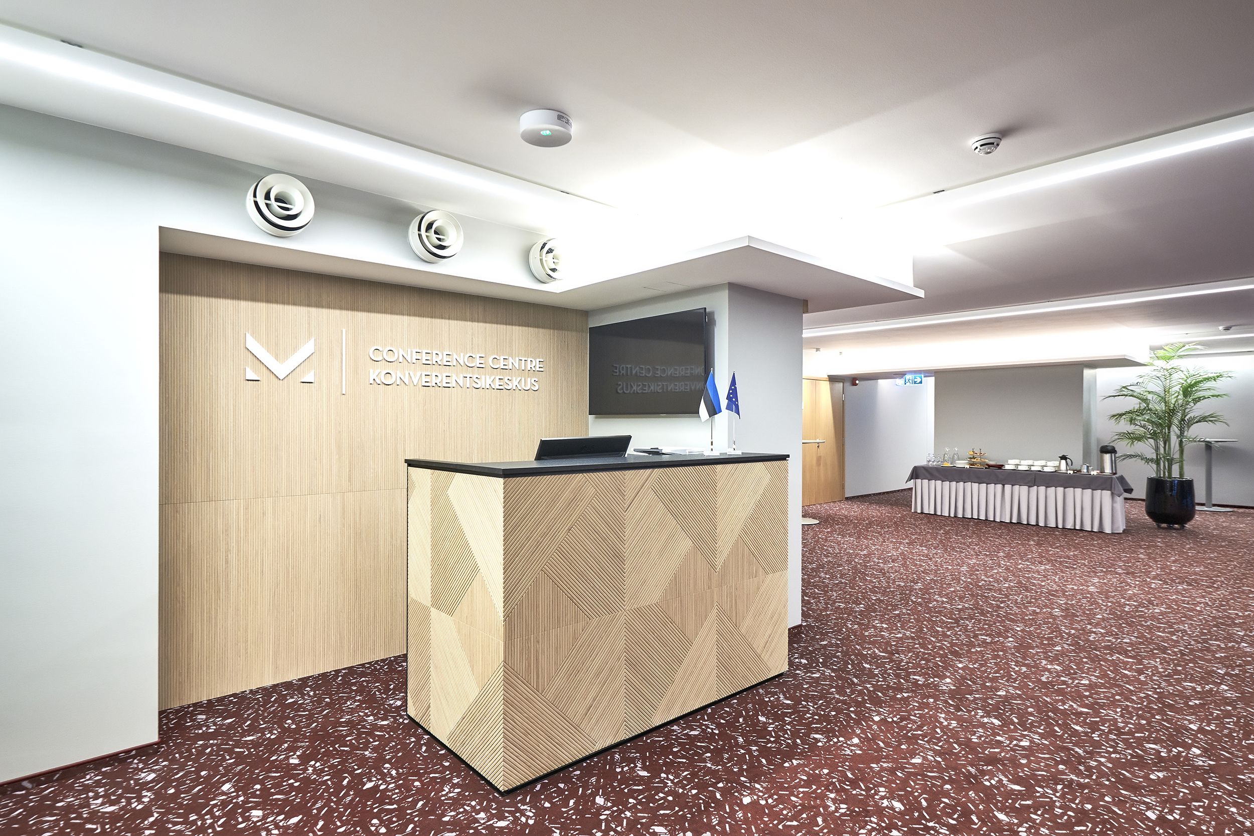 Ein Empfangsbereich mit einem Holztresen, einem Fernsehbildschirm und einem Schild für das Konferenzzentrum.