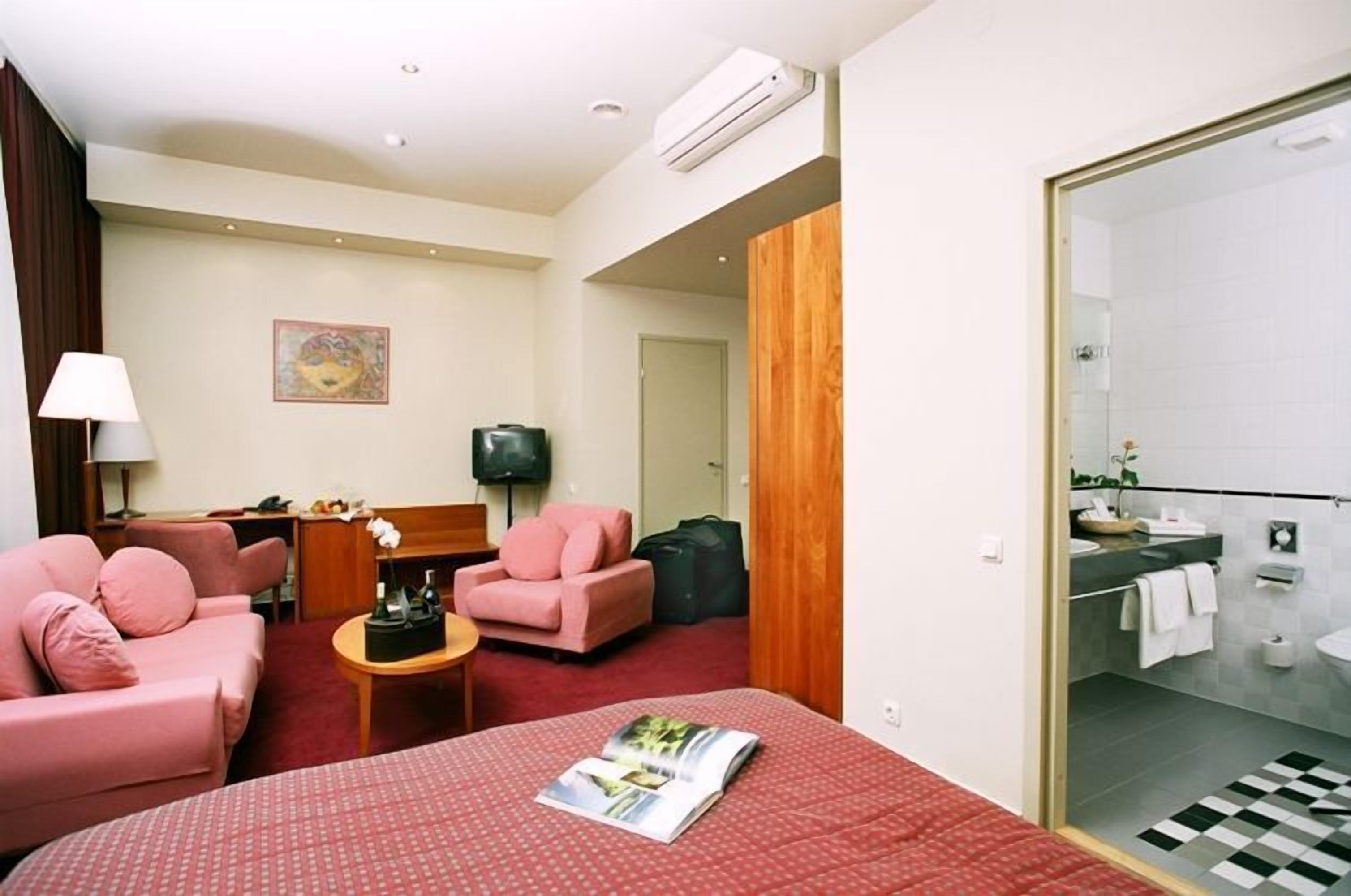 A hotel room with a bed, a desk, a chair, a sofa, a TV, and a bathroom.
