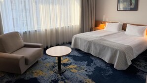 Una habitación de hotel con cama, una silla, una mesa redonda y un cuadro en la pared.