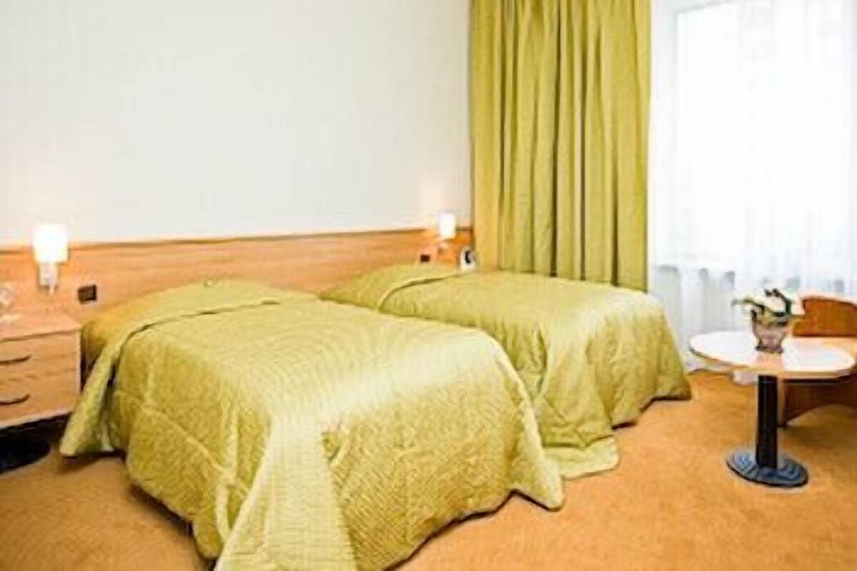 Hotellihuone, jossa on kaksi erillistä sänkyä, pieni pyöreä pöytä ja ikkuna, jossa on verhot.