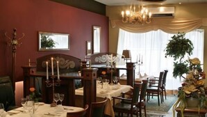 Comedor con mesas dispuestas para una comida, una araña y un ventanal con cortinas.