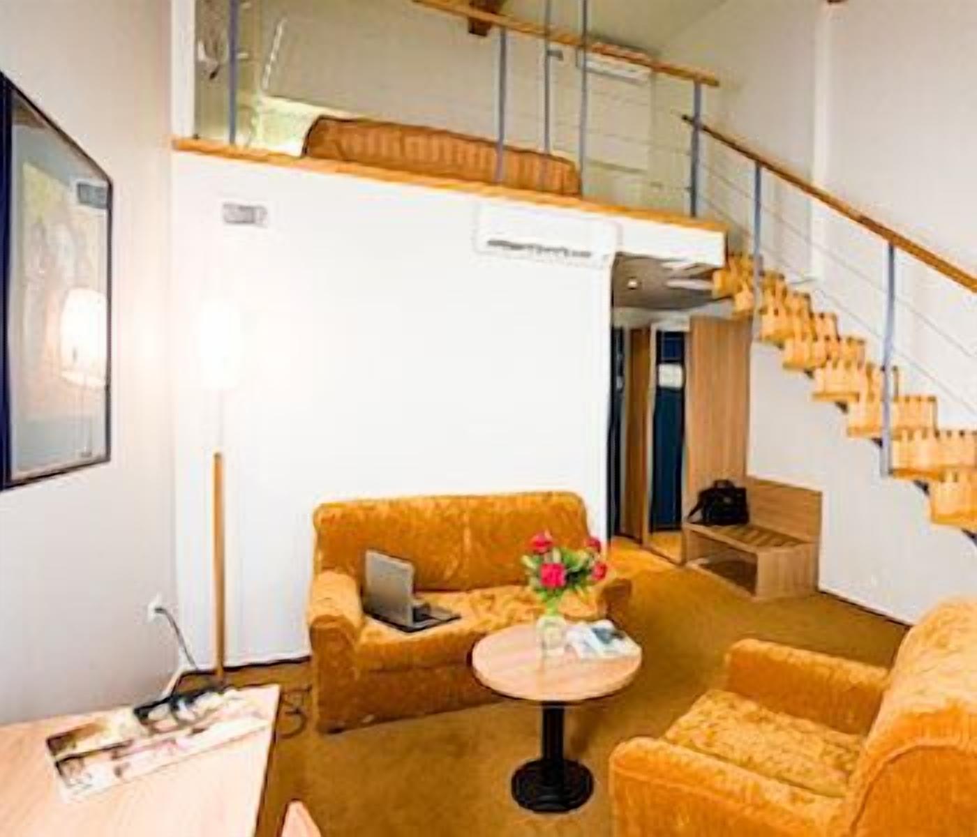 A hotel room with a sofa, a small round table with a vase of flowers, a laptop on the sofa, and a staircase with wooden steps.