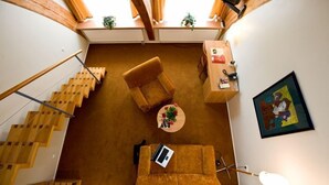 Amplia sala de estar con escalera de madera, un sofá, una mesa de centro y un cuadro en la pared.