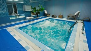 Una piscina interior con suelo y paredes de azulejos azules, rodeada de sillones de descanso y una planta en maceta.