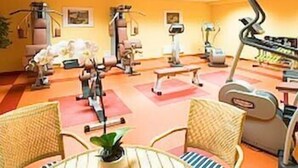 Un gimnasio con equipo de ejercicio, incluyendo cintas de correr y bicicletas estáticas, y un área de descanso con sillas y una mesa.