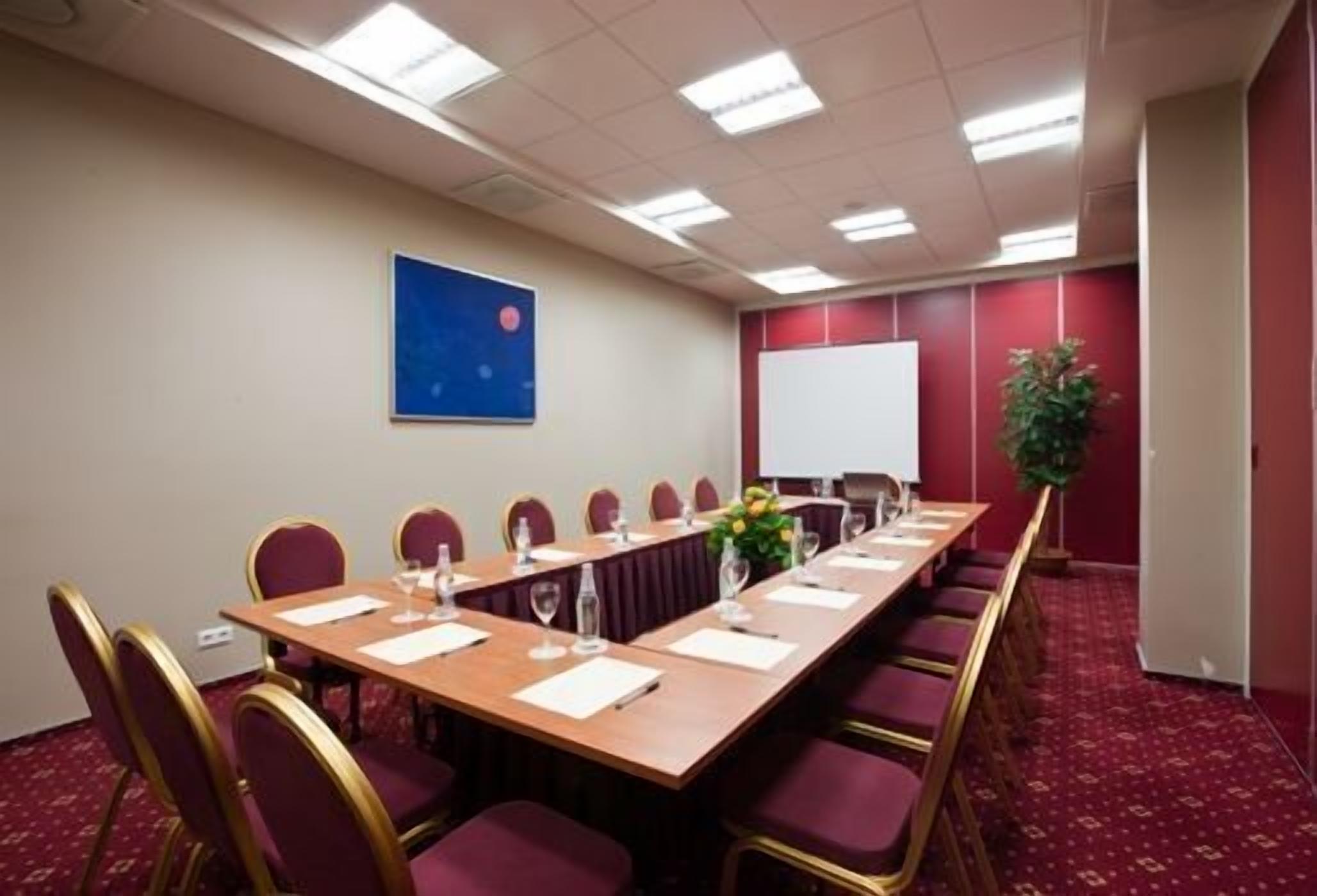 A conference room with a long table, chairs, a whiteboard, and a projector screen.