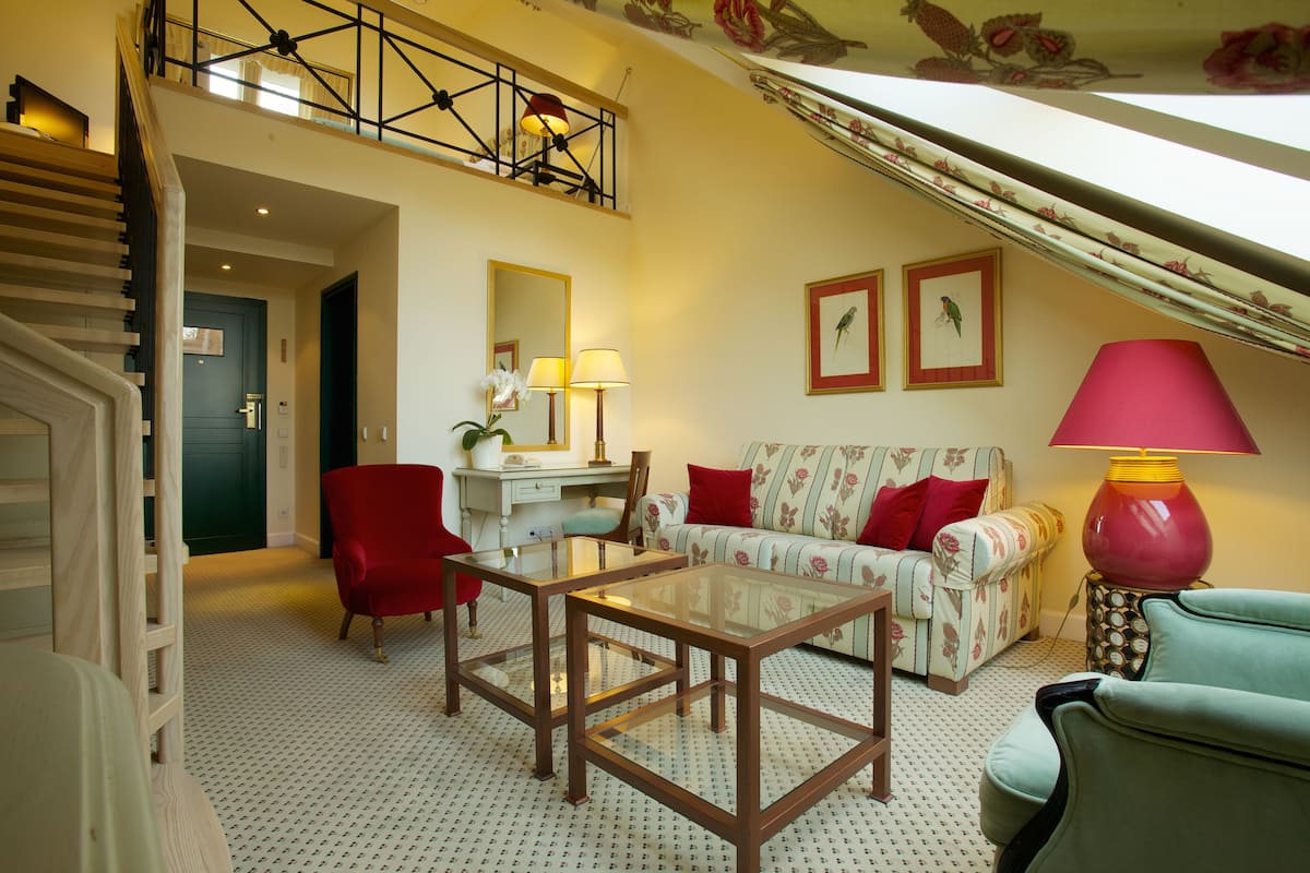Amplia sala de estar con escaleras, un conjunto de sofás, una mesa de centro de vidrio y una lámpara roja.