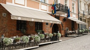 Un bâtiment historique à la façade en briques, portant le numéro 24, doté d’une terrasse avec des parasols blancs et des garde-corps en fer forgé noir.